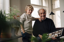 Grandfather Showing Butterfly Collection To Grandson At Home