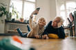 © Westend61 - Grandfather and grandson lying on the floor at home taking a selfie