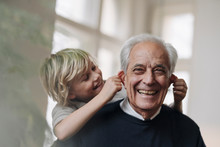 Happy Grandson Pulling Grandfather's Ears At Home