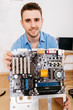 © Westend61 - Portrait of smiling technician holding the mainboard of a computer