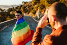 Photographer Taking Picture Of Man Wrapped In A Gay Pride Flag On A Road In The Mountains