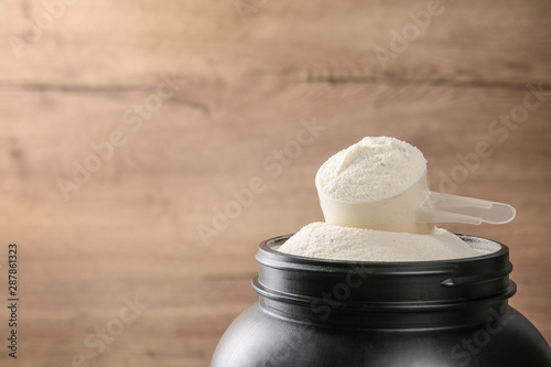 Cuadros en Lienzo Black jar with measuring scoop of protein powder against wooden background