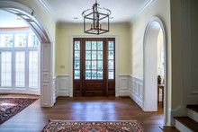 Front Entrance Foyer Hallway Of A Large Home House With Yellow Walls And A Wood Door With Windows And A Large Custom Lighting Fixture