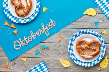 Wall Mural - Oktoberfest rustic background with prezels in paper plates, paper flags and Autumn leaves