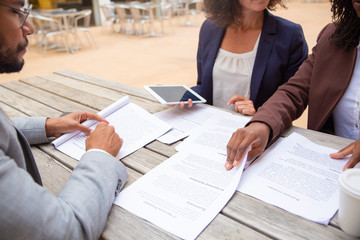 Legal experts reviewing customer documents in street cafe. Business man and woman sitting at table with takeaway coffee, reading papers, using tablet. Paper expertise concept