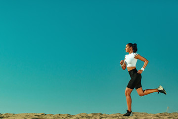 Wall Mural - Sporty young woman and fit athlete runner running on the sky background. The concept of a healthy lifestyle and sport. Woman in black and white sportswear.