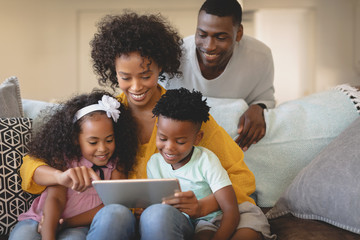 Wall Mural - African American mother with her children using digital tablet on sofa while father looking them