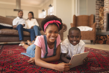 Wall Mural - African American sibling lying on floor with digital tablet and looking at camera