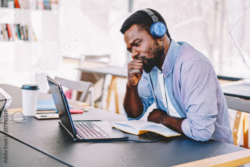 Young african american hipster guy in headphones watching online football match worried and nervous about team, african american hipster guy concentrated on training webinar learning online course.
