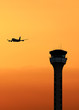 Air traffic control tower with an airplane taking off at sunset