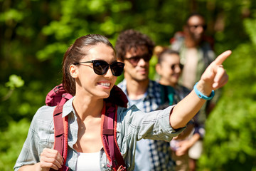 travel, tourism, hike and people concept - woman showing something to group of friends walking with backpacks in forest