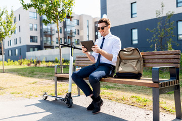 Poster - business, technology and people concept - young smiling businessman with tablet computer, backpack and electric scooter sitting on street bench in city