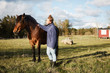 © Maskot - Side view of mid adult woman stroking horse while standing on grassy field against sky