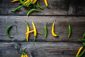 Wall Mural - Word CHILI made of raw organic yellow and green chili cayenne peppers on old wooden table