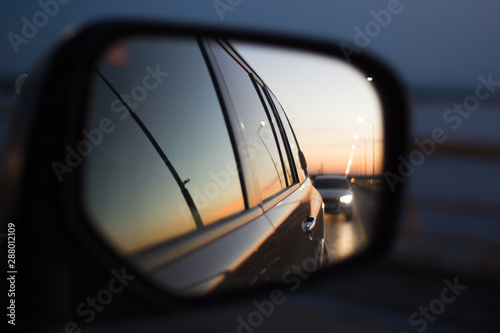 Fotografía side mirror of a car in which a road with a traveling car is reflected at sunset