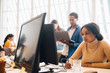 © Maskot - Focused businesswoman using computer while coworkers working in background at office