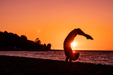 Flexible Woman Practicing Yoga On The Beach With A Pink Sunset, Reflections In The Water, Wellbeing, Zen Attitude, Healthy And Tranquility