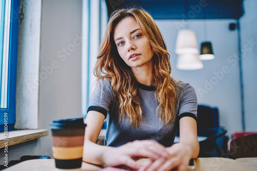 Fotomural Portrait of thoughtful hipster girl sitting at table with takeaway caffeine beve