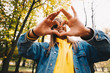 © PinkCoffee Studio - Woman portrait. Autumn walk. Happy  girl in jean jacket and sunglasses is showing a heart at camera and smiling while walking in the park