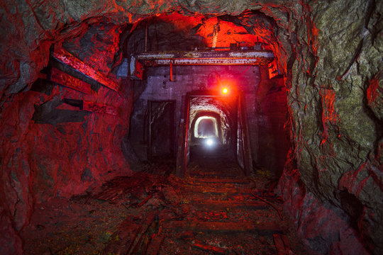 Dark dirty abandoned uranium mine with rusty remnants of railway color illuminated