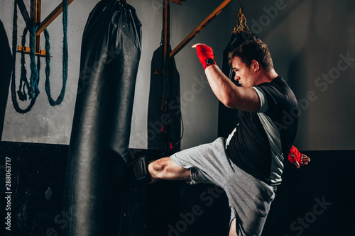 Muscular kickbox fighter exercising with punch bag at the gym Фотошпалери
