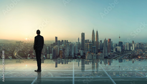 Businessman standing at transparent glass floor on rooftop with city skyline, success and thinking concept  .