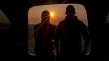 A man and a woman admire the beautiful sunset from the trunk of a car