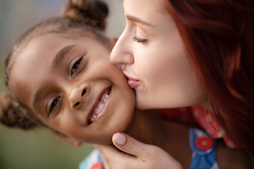 Wall Mural - Adopted girl smiling broadly while mother kissing her