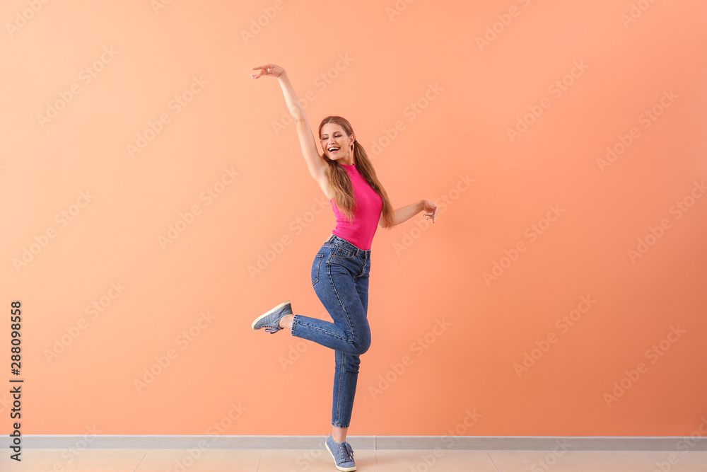 Beautiful young woman dancing against color wall