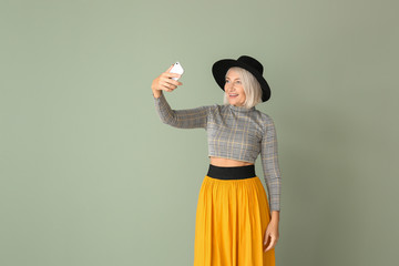 Wall Mural - Stylish mature woman taking selfie on color background