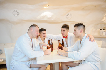 close up photo of 4 men in white gowns sitting around a table and drinking beer after sauna procedures