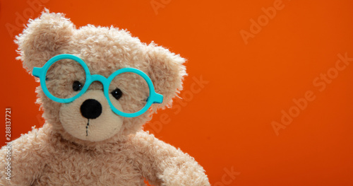 Fotografía Cute teddy wearing eyeglasses against orange color background