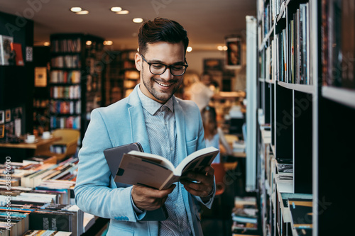 Photographie Middle age man choosing and reading books in modern bookstore.
