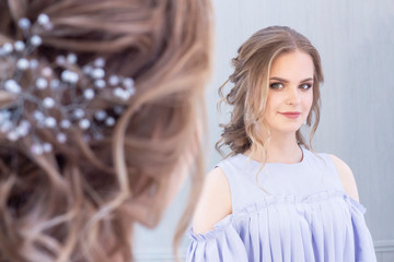 beautiful girl with a wedding hairstyle looks at herself in the mirror, portrait of a young girl. beautiful make-up. beauty saloon