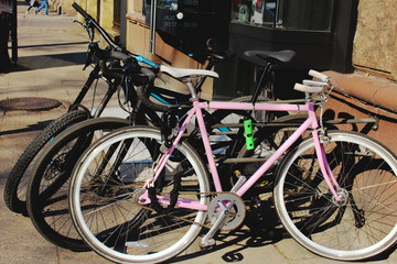 Two black and a pink bicycle parked on city street