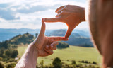 Rear view of Man looking at mountain landscape framing with fingers, searching for best image composition as he hiking over the mountain range. Landscape photographer or moviemaker occupation concept.
