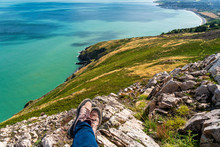 Resting On The Rocky Cliff Edge On A Sunny Day And Enjoying The Beautiful View Of The Irish Sea. Coastal Landscape From Above The Famous Bray Head Cliff Walk In Greystones, Wicklow, Ireland.