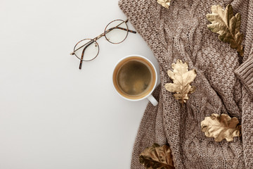 Wall Mural - top view of knitted sweater, glasses, coffee and golden foliage on white background