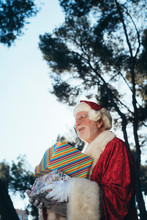 From Above Cheerful Man In Costume Of Santa Claus Standing With Gifts By Turquoise Van On Nature Background In Summer Looking Away