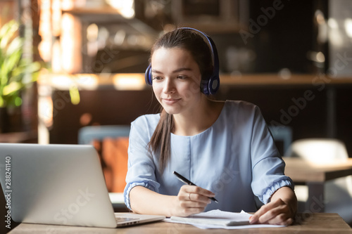 Fotografía Focused woman wearing headphones using laptop, writing notes