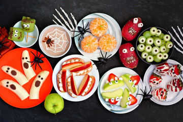 Wall Mural - Healthy Halloween fruit snacks. Selection of fun, spooky treats. Top view table scene over a black stone background.