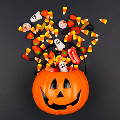 Wall Mural - Halloween Jack o Lantern pail with spilling candy, top view on a black background