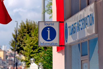 tourist information sign with information symbol hanged in front of an information desk. trees and p