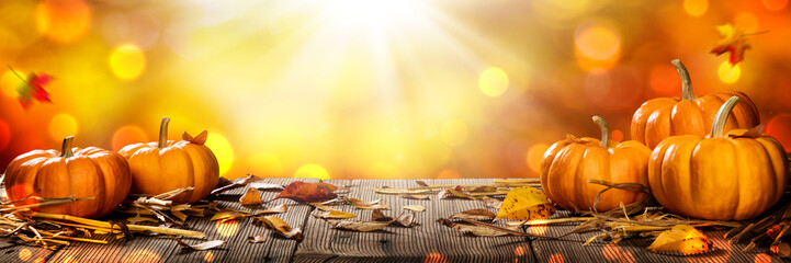 Wall Mural - mini thanksgiving pumpkins and leaves on rustic wooden table with sunlight and bokeh on orange backg