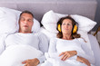 Woman Covering Her Ears With Headphones While Man Snoring