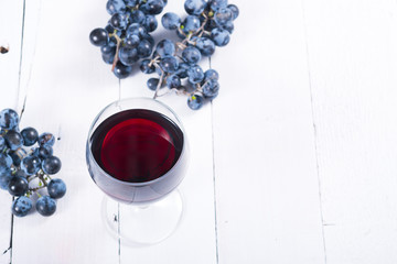 Wall Mural - glass of red wine and blue grapes on white wooden table background