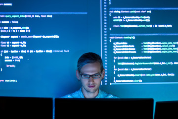 Software developer freelancer man male work with program code C++, Java, Javascript on wide displays at night. Develops new web desktop mobile application or framework. Projector futuristic background