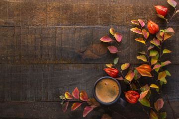 Canvas Print - Dark brown clay cup with black coffee and branches of autumn leaves (Spiraea Vanhouttei) with Physalis on the old wooden table. Top view.