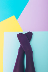 Wall Mural - Women's legs in purple tights on a geometric colored background. Flat lay