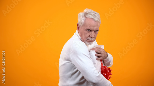 Cuadros en Lienzo Greedy male pensioner embracing giftbox and seriously looking on camera, avarice